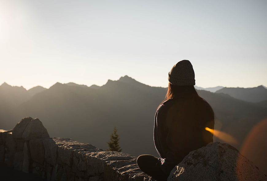 Woman sitting on mountain peak watching sunset