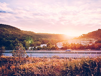 Car Driving on Highway Through Forested Hills at Golden Sunset