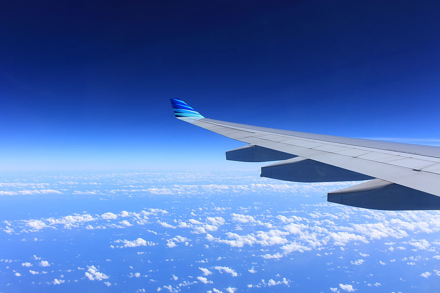 Airplane Wing View Above Clouds in Blue Sky