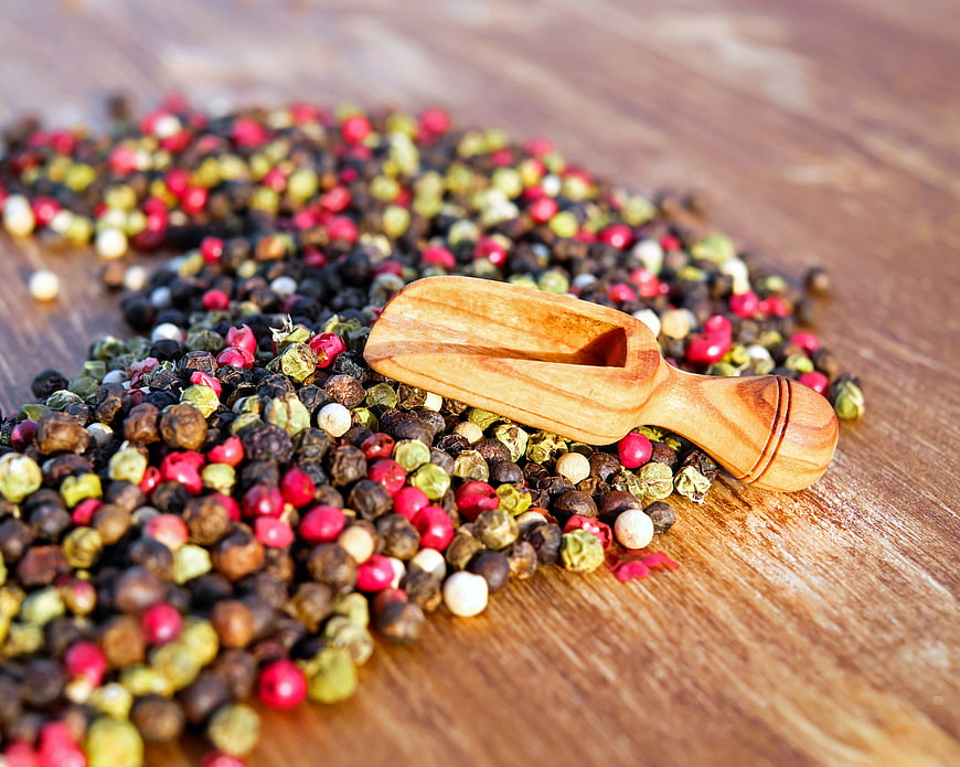 Colorful peppercorns and wooden scoop on rustic wood