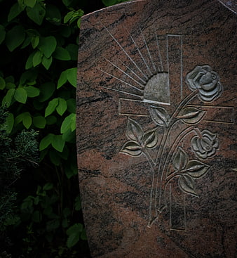 Close-up of carved cross and roses on red granite tombstone