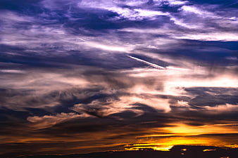 Dramatic sunset sky with purple clouds and airplane contrail