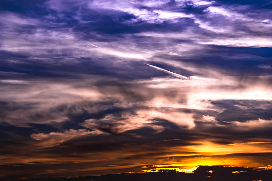 Dramatic sunset sky with purple clouds and airplane contrail
