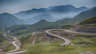 Winding Mountain Road Through Green Hills and Misty Peaks
