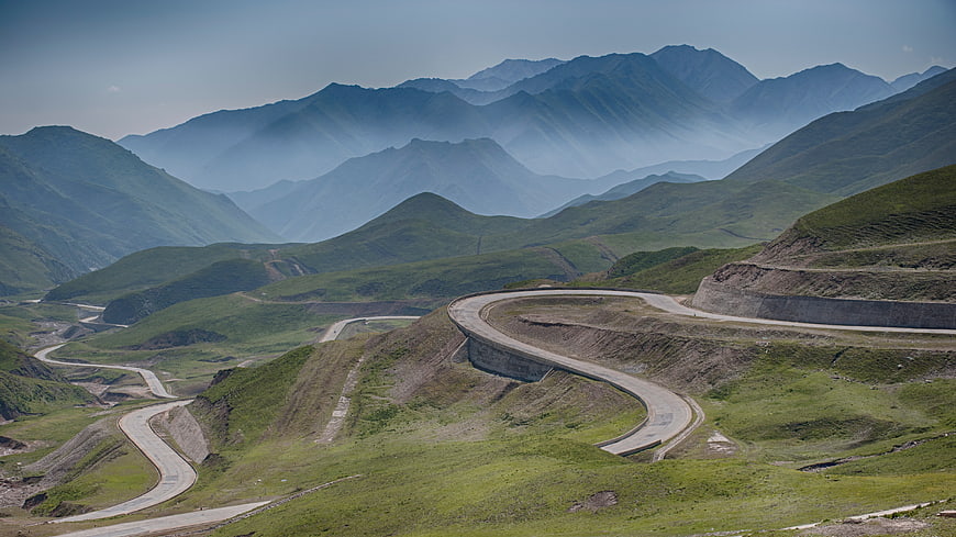 Winding Mountain Road Through Green Hills and Misty Peaks