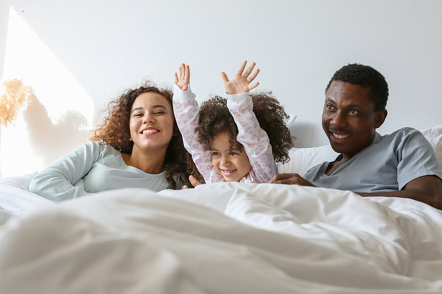 Happy family in bed with child raising hands