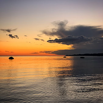 Serene Sunset Over Calm Ocean with Silhouetted Rocks