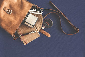 Flat Lay of Brown Leather Bag with Accessories on Blue Background