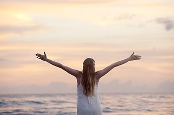 Woman with arms raised facing ocean sunset