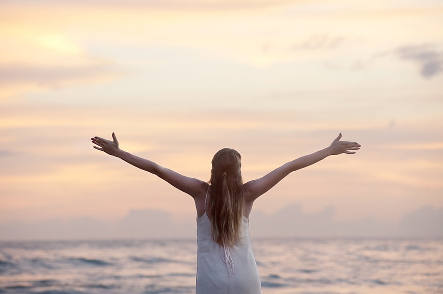 Woman with arms raised facing ocean sunset