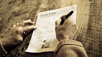 Senior hands solving crossword puzzle on wooden table