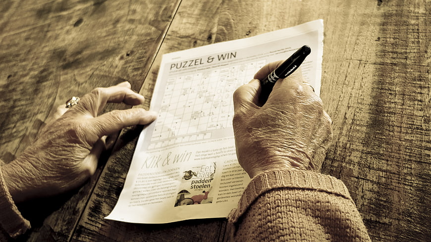Senior hands solving crossword puzzle on wooden table