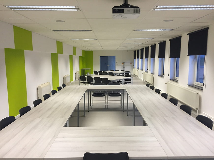 Modern empty classroom with green walls and white desks
