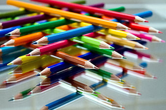 Colorful wooden pencils scattered on reflective surface