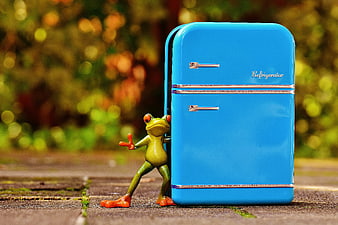 Cute Green Frog Figurine Leaning Against Blue Miniature Refrigerator