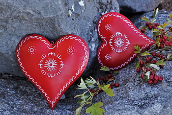 Two red heart-shaped ornaments with white embroidery on a rocky surface