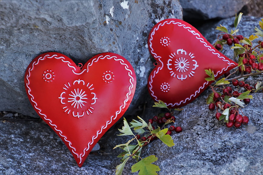 Two red heart-shaped ornaments with white embroidery on a rocky surface