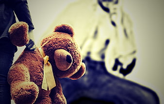 Child holding teddy bear with distressed adult in background