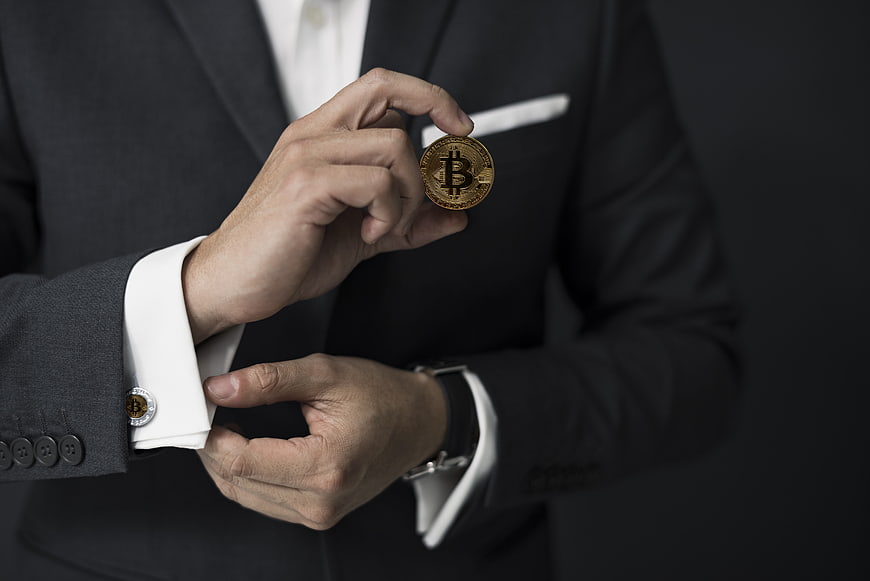 Businessman in dark suit holding physical gold bitcoin coin