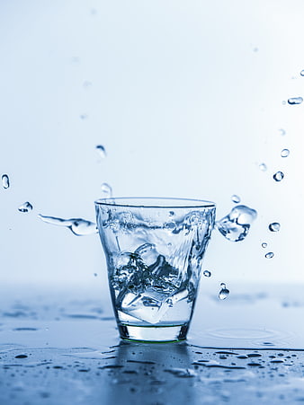 Glass of Ice Water with Splashing Droplets on Blue Background