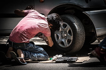 Young man repairing car tire with tools on cardboard