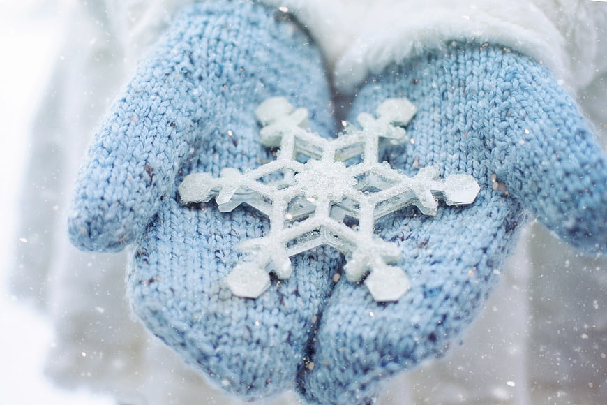 Blue Knitted Mittens Holding a Snowflake in Winter Snow