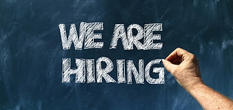Hand writing We Are Hiring in white chalk on a dark blue blackboard