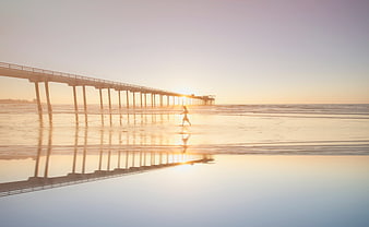 Child Running on Beach at Sunset with Pier Reflection