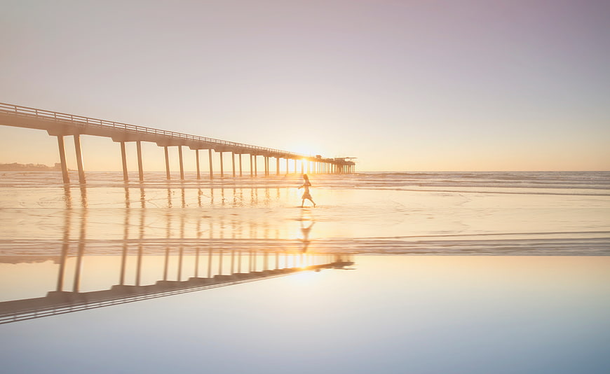 Child Running on Beach at Sunset with Pier Reflection