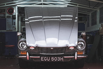 Front view of vintage silver car with open hood in garage
