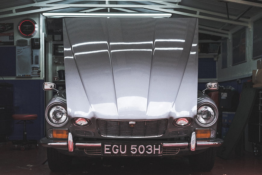 Front view of vintage silver car with open hood in garage