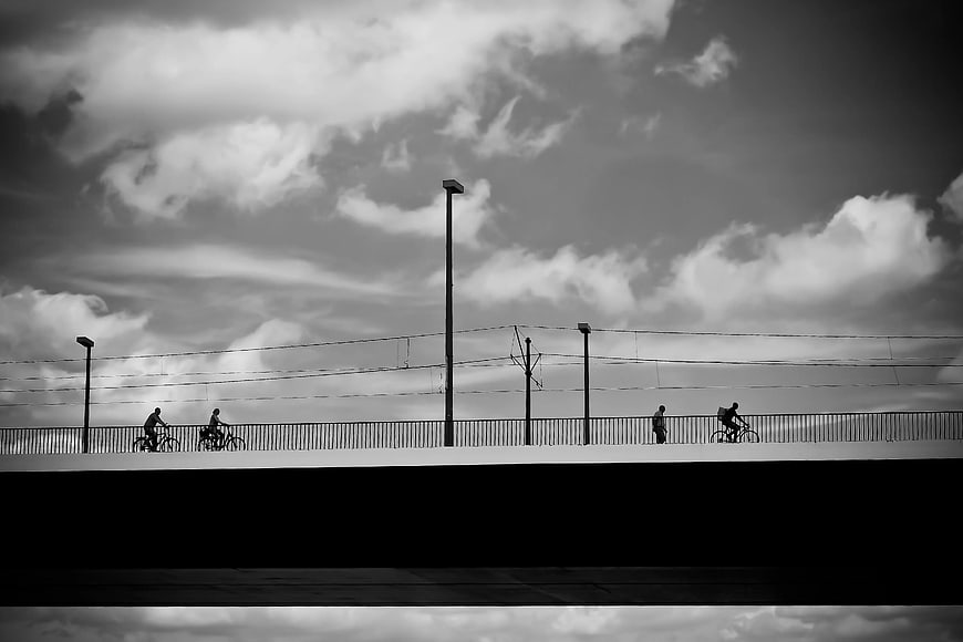 Silhouettes of Cyclists on Bridge Against Dramatic Sky