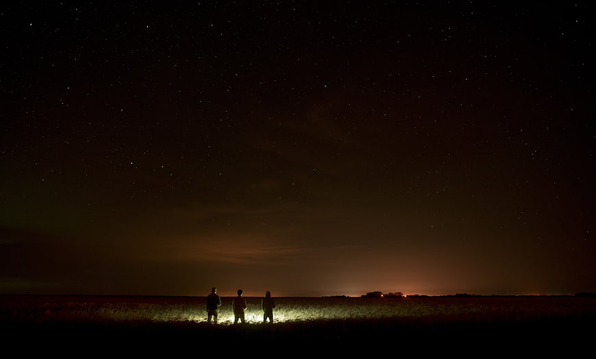 Three Silhouetted Figures Stargazing in a Field at Night