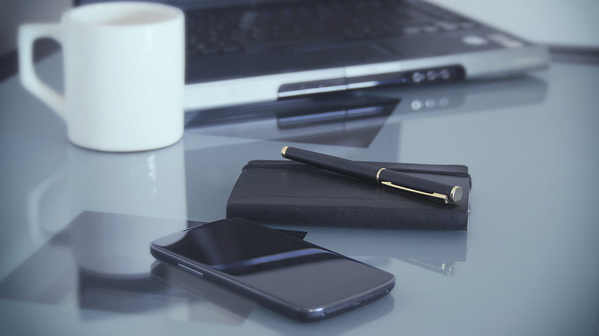 Modern office desk with laptop, smartphone, notebook, and coffee cup