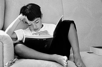 Young boy reading book on sofa in black and white