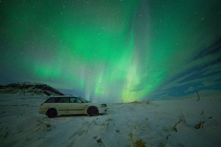 White car parked in snow under green aurora borealis