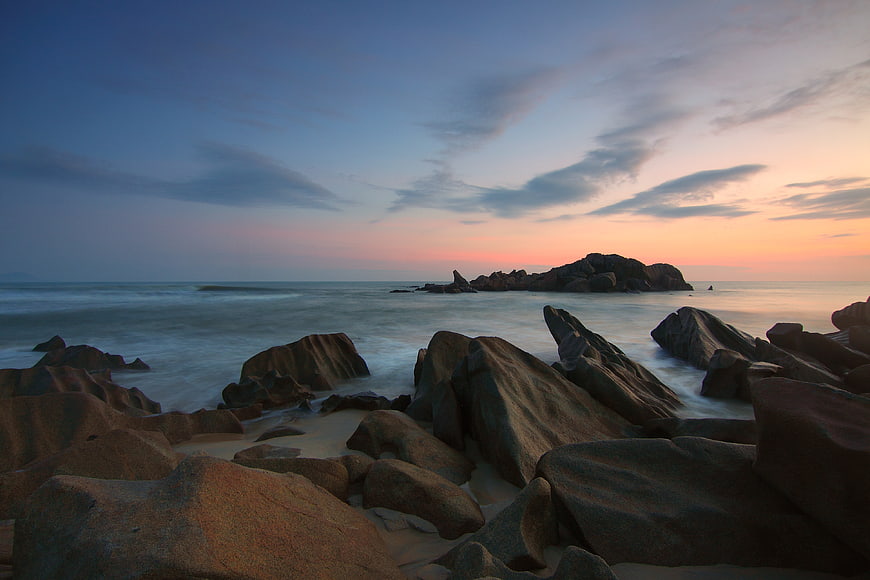 Serene Sunset Over Rocky Coastal Beach with Smooth Ocean Waves