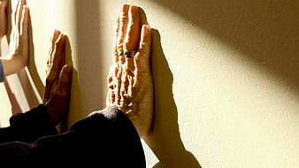 Senior hands pressed against wall in sunlight