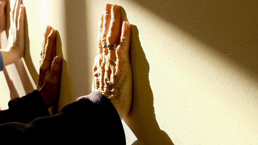 Senior hands pressed against wall in sunlight