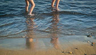 Children's legs walking in shallow ocean water at sunset