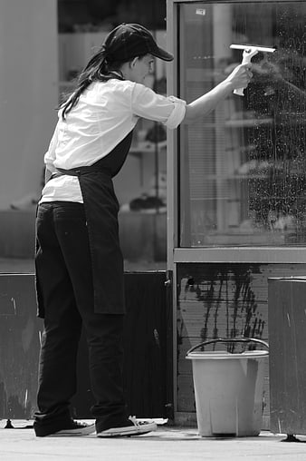 Woman cleaning glass storefront window with squeegee and bucket
