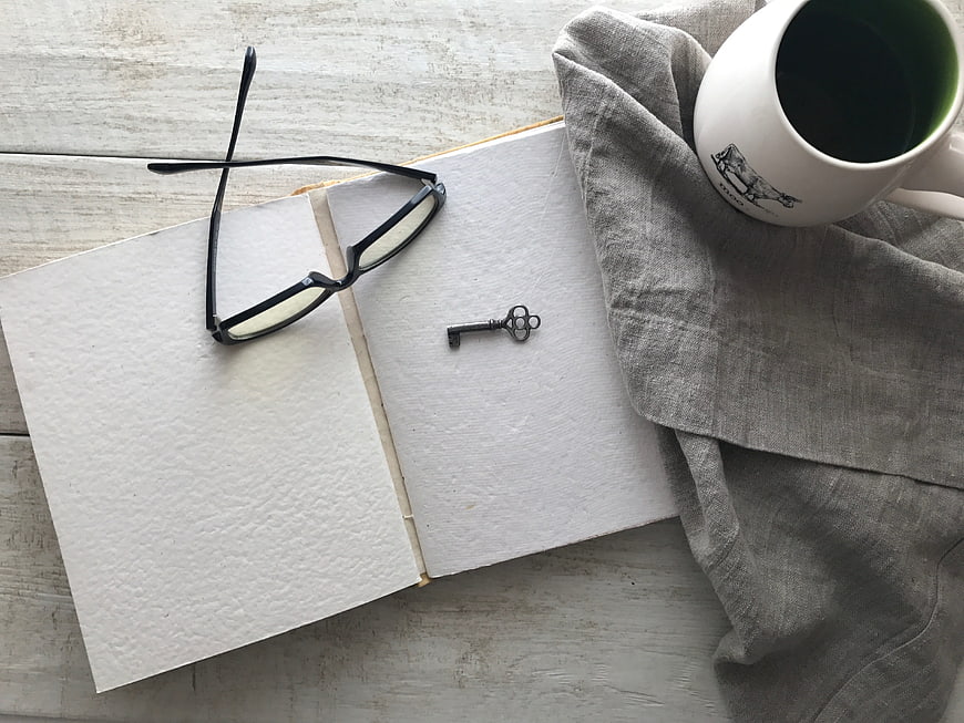 Flat lay of open book, glasses, key, and coffee mug