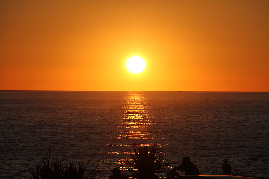 Silhouette of people watching vibrant orange sunset over ocean