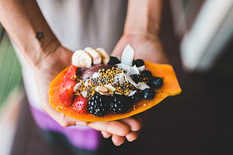 Hands holding healthy papaya fruit bowl with berries and seeds