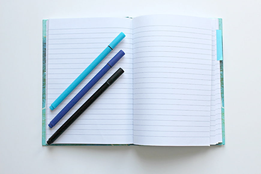 Open Notebook with Blue and Black Pens on White Background