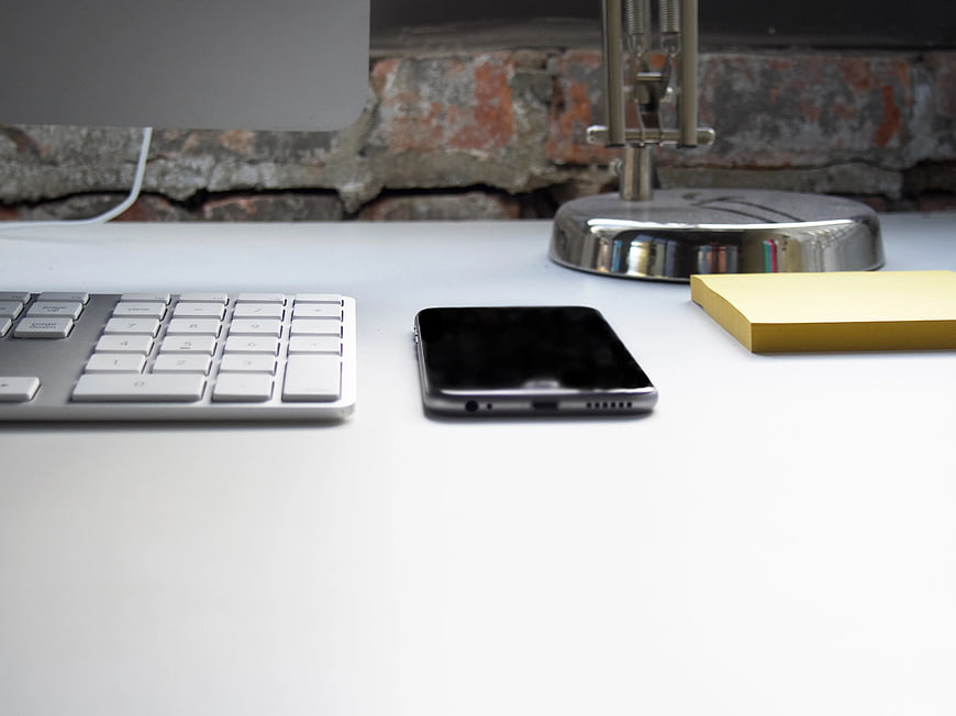 Minimalist White Desk with Keyboard, Smartphone, and Yellow Notepad