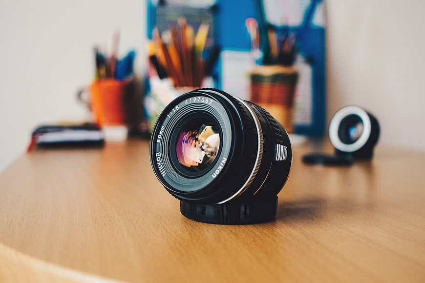 Nikon Camera Lens on Wooden Desk with Stationery