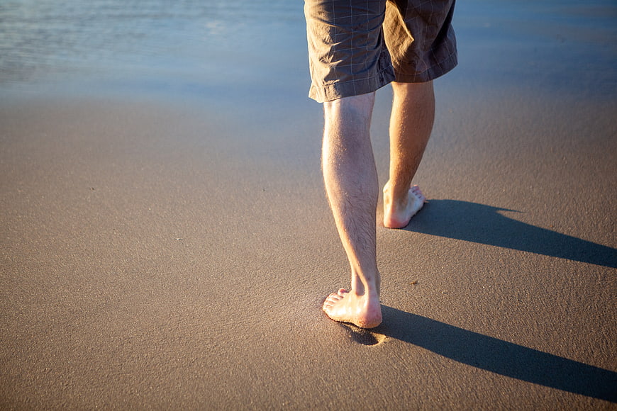 Barefoot Man Walking on Sandy Beach at Sunset