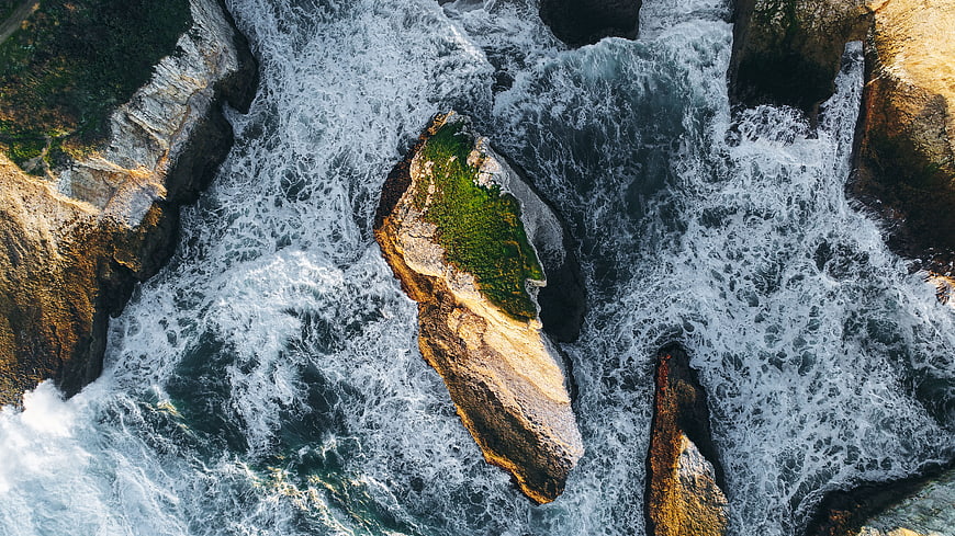 Aerial view of crashing ocean waves against rocky coastline