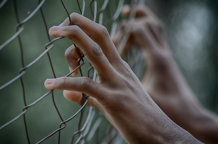 Close-up of hands gripping a wire mesh fence